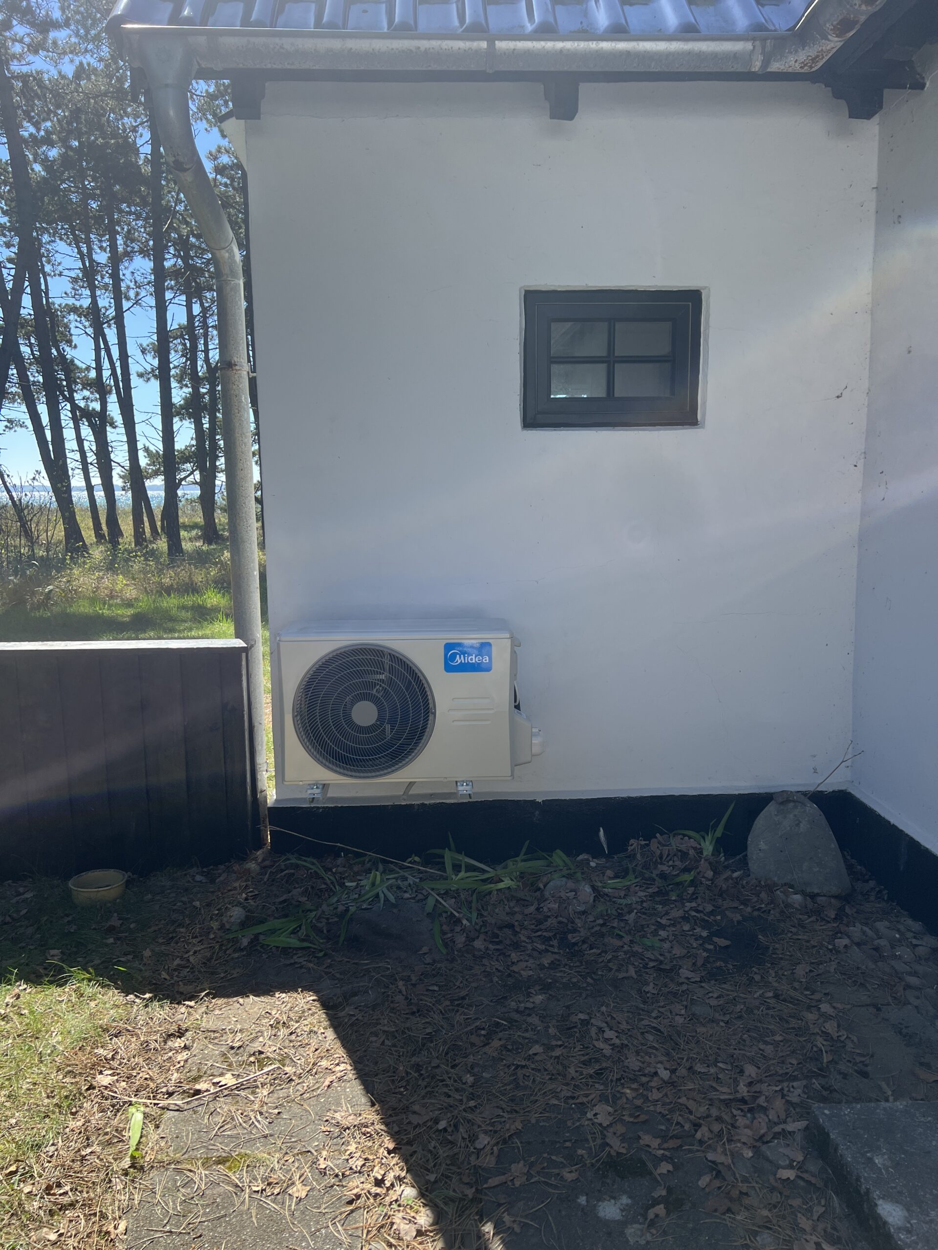 Midea udedel ved et sommerhus med hvid træfacade.
